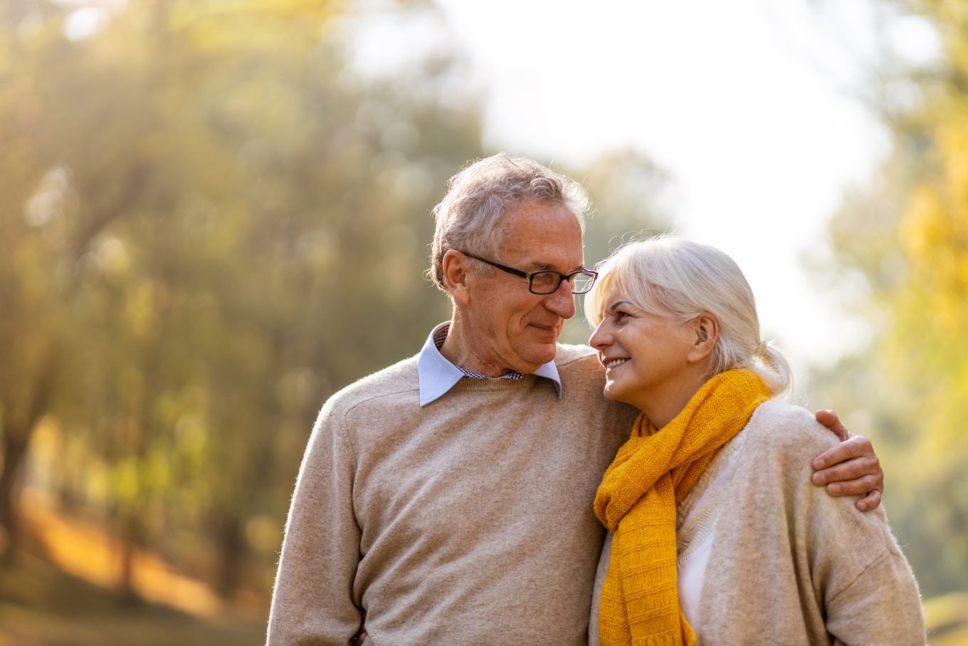 An older white couple embraces in an outside setting. 