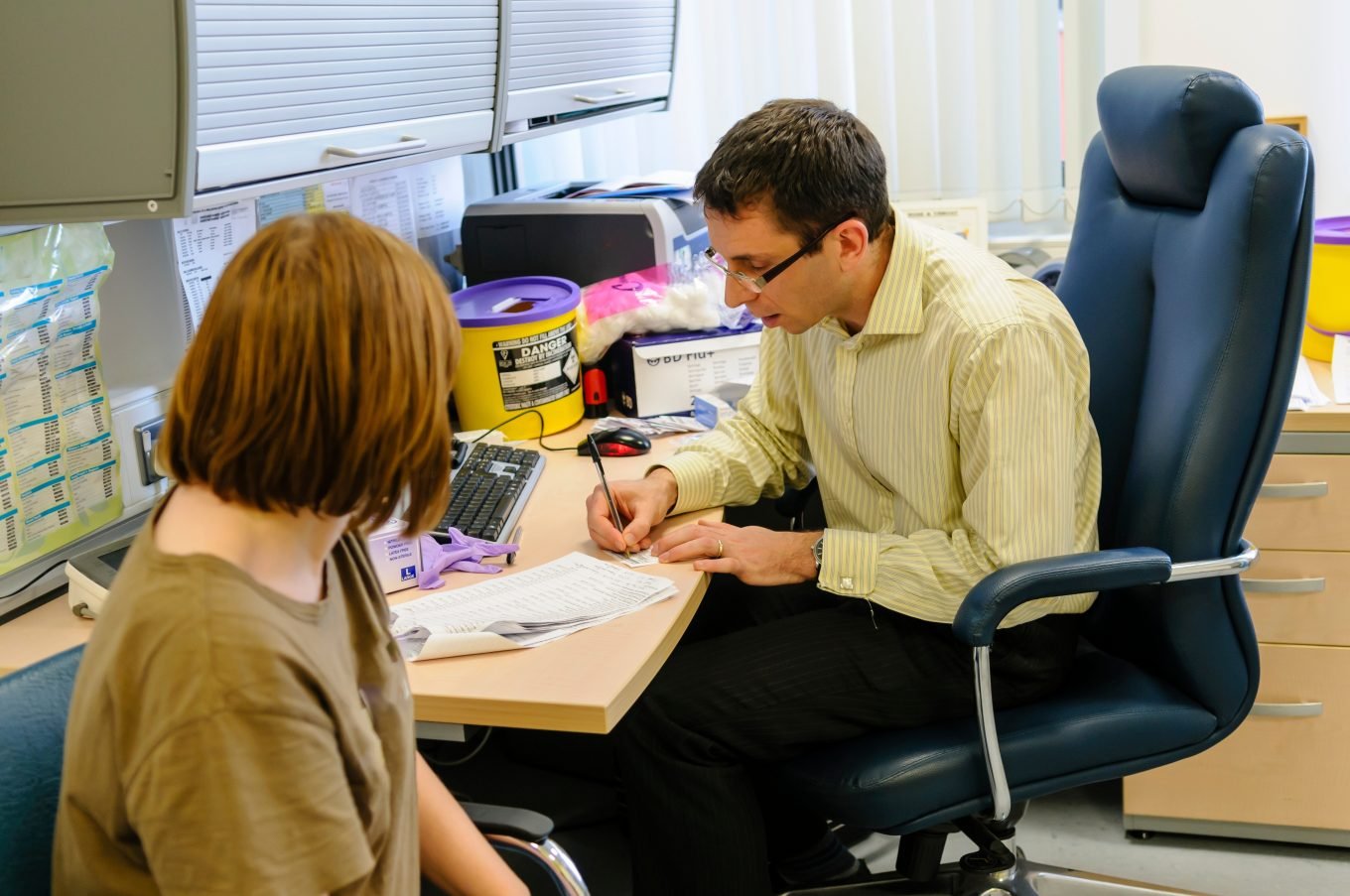 A brown, male personal trainer consults a clipboard with test results during a training session with a white, female client, who is holding a water bottle. The photo aims to illustrate the benefits and limitations of fitness testing in a personal training context.