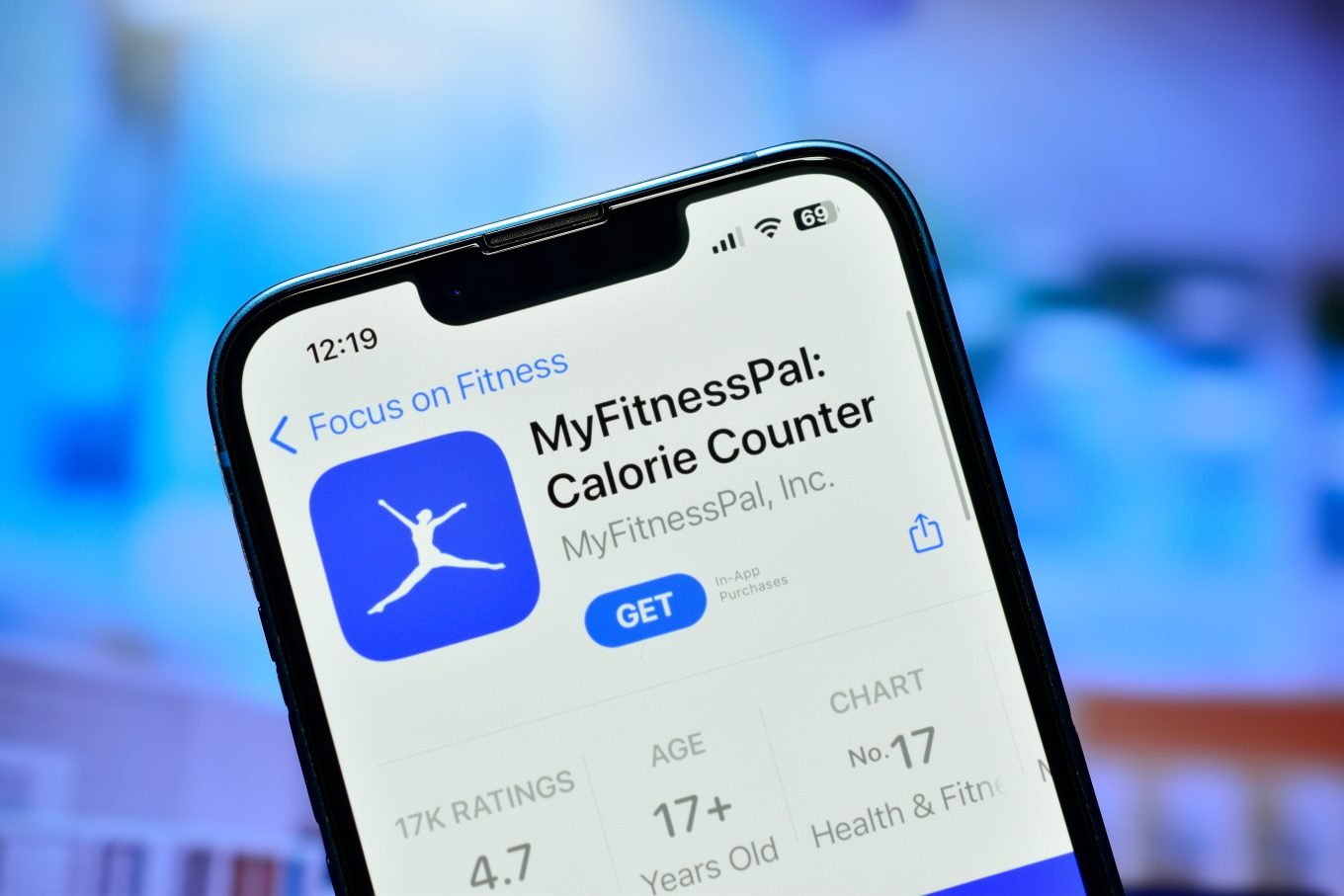 A phone screen displays the app store page for "MyFitnessPal: Calorie Counter" against a blurred blue background. 