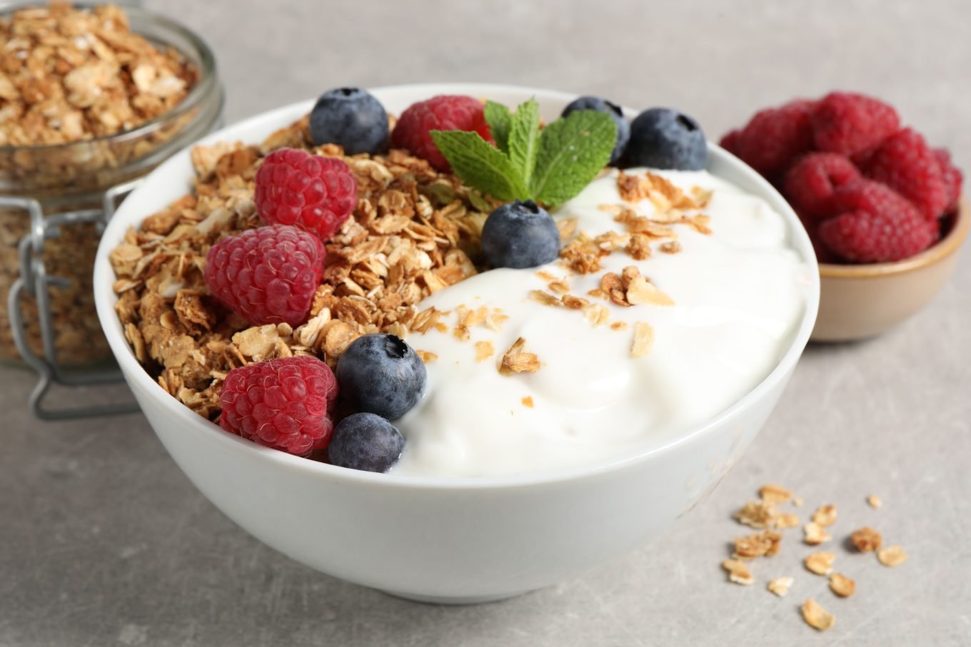 Greek yoghurt in a white bowl paired with granola, fresh fruits, and a mint leaf. 