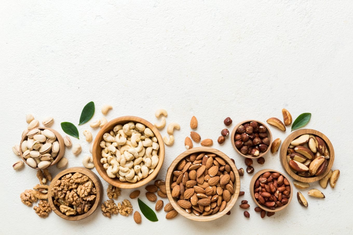 A variety of healthy nuts are displayed in bowls and on a table. 