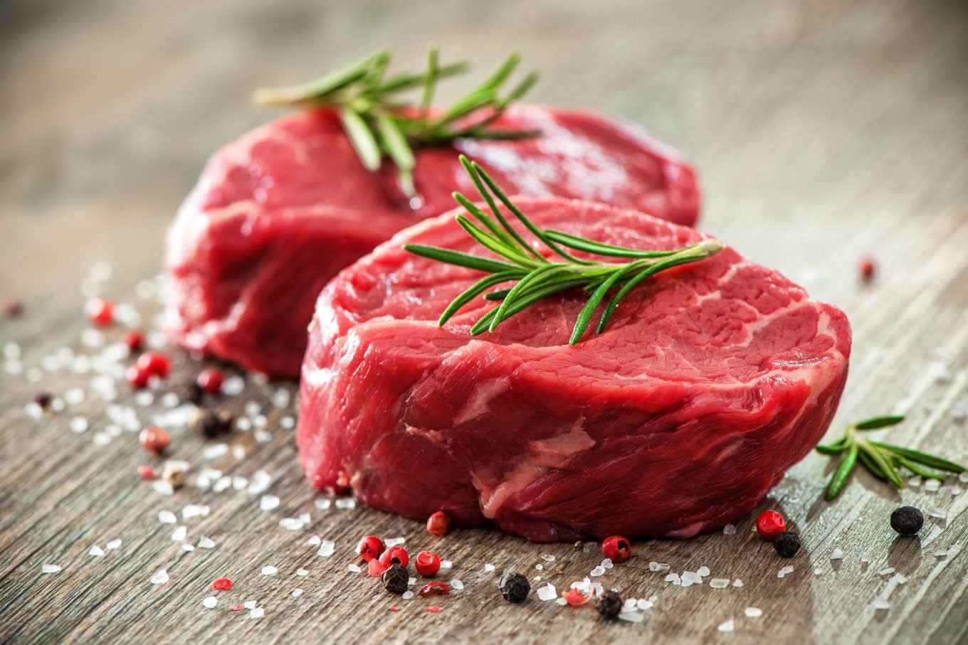 Two raw beef filet steaks with fresh rosemary, sea salt, and black pepper. 